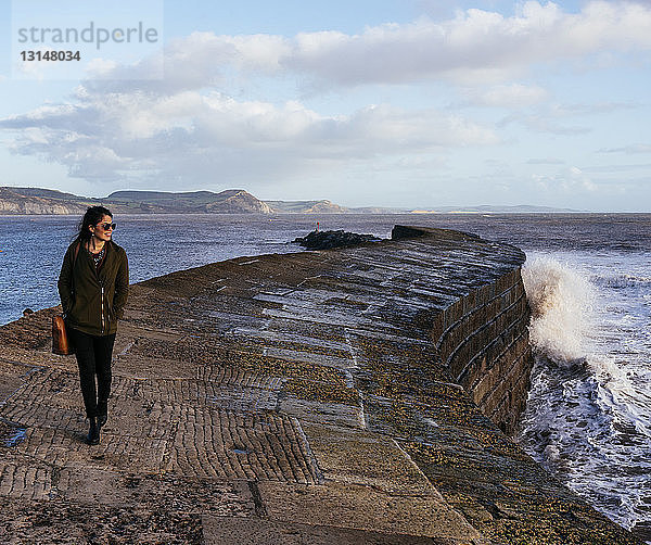 Junge Frau  die an der Hafenmauer The Cobb entlang spaziert  Lyme Regis  Dorset  England