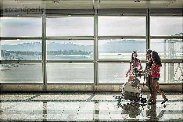 Teenager-Mädchen und Frau schieben Gepäckwagen im Flughafen