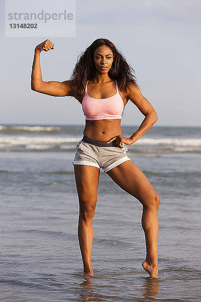 Junge Frau am Strand  Muskeln anspannen  posieren