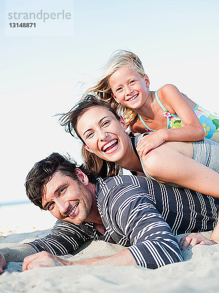 Familie liegt lächelnd im Sand am Strand