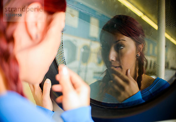 Junge Frau im Waschsalon  die ihr Spiegelbild in der Waschmaschine betrachtet