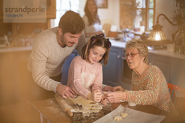 Eine Familie in der dritten Generation schneidet Formen in den Teig  um selbstgebackene Kekse herzustellen