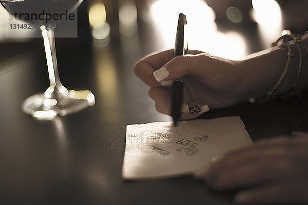 Nahaufnahme einer jungen Frau  die ihre Telefonnummer auf eine Serviette in einer Bar schreibt