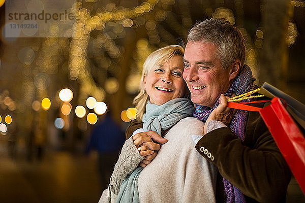 Porträt eines reifen Paares mit Weihnachtseinkäufen auf einer von Bäumen gesäumten Allee  Mallorca  Spanien