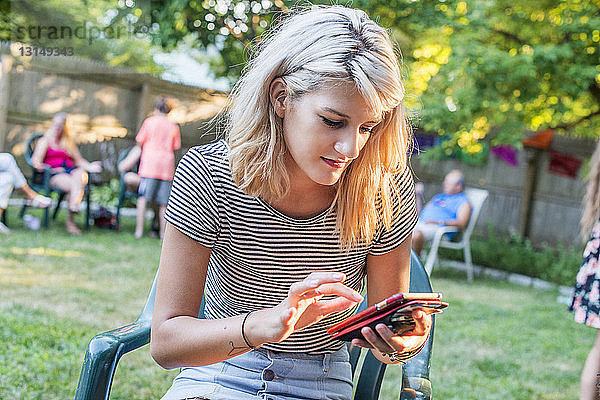 Junge Frau  die auf einer Party im Garten eine SMS auf ihrem Smartphone schreibt