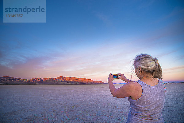 Frau fotografiert mit ihrem Smartphone die Salinen und die entfernten Berge bei Sonnenuntergang  Calico  Kalifornien  USA