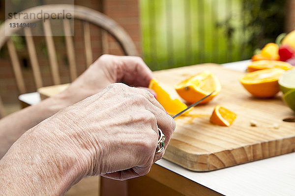 Hände einer älteren Frau beim Schneiden von Orangen am Gartentisch