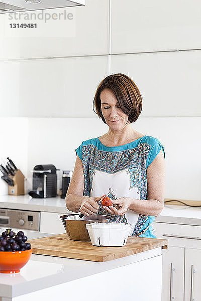 Reife Frau bereitet Erdbeeren in der Wohnküche zu