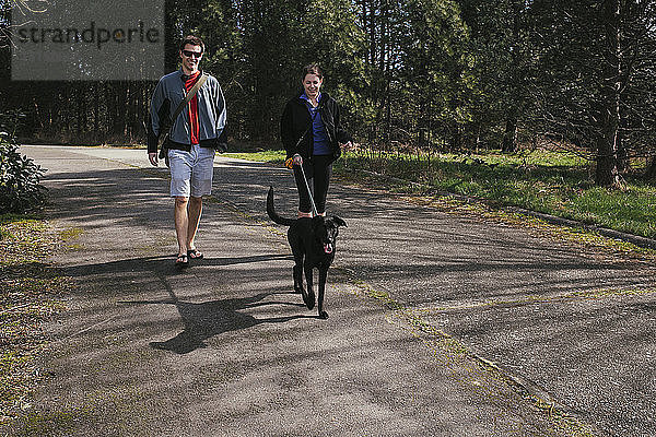 Ehepaar geht mit Hund im sonnenbeschienenen Park spazieren