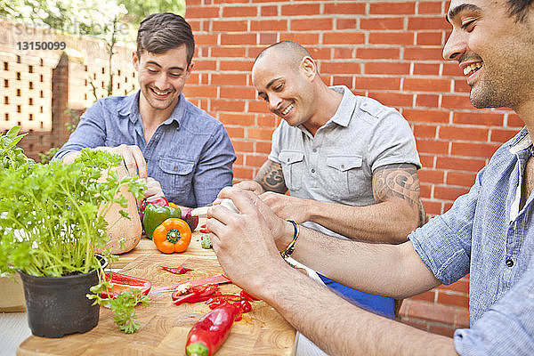Drei männliche Freunde lachen und bereiten Essen für ein Grillfest im Garten vor