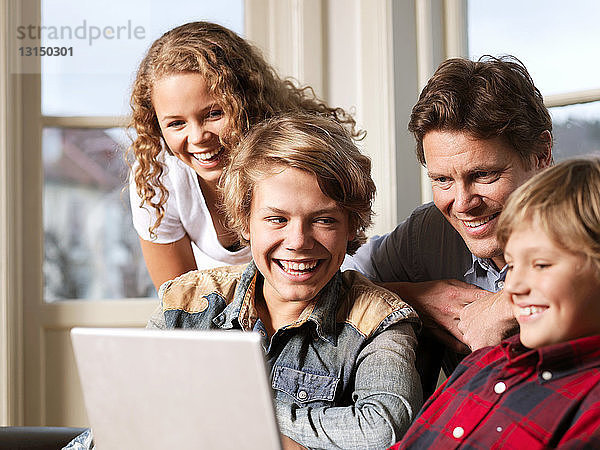 Vater schaut Laptop mit Söhnen und Tochter auf dem Sofa