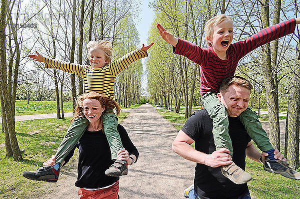 Mutter und Vater rasen mit zwei Jungen auf den Schultern durch den Park