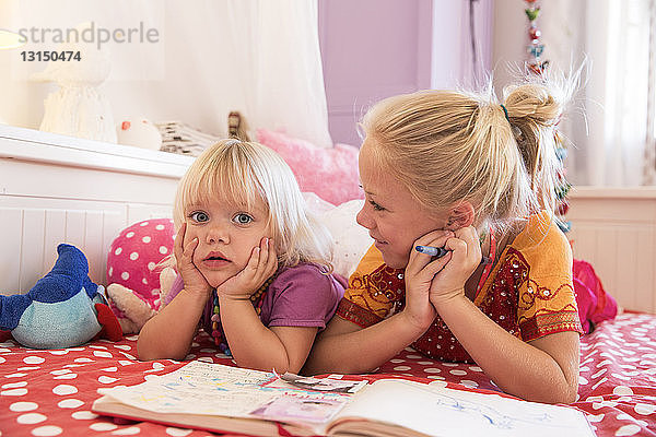 Mädchen und Kleinkind Schwester auf Bett spielen mit Malbuch