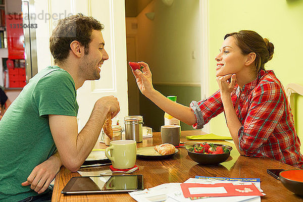 Junges Paar beim Frühstück  Frau füttert Mann mit Erdbeeren