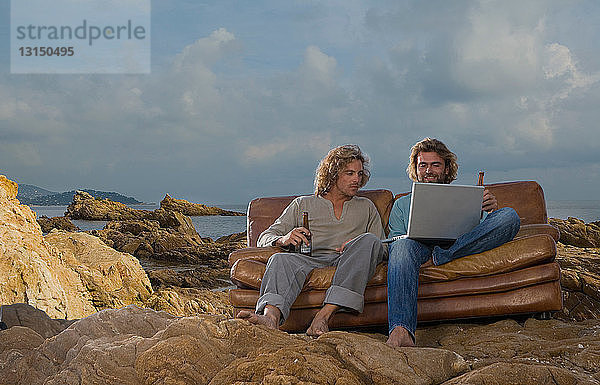 Männer mit Laptop und Bier auf Couch  Strand