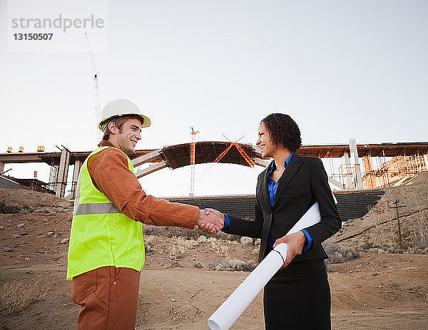 Mann und Frau schütteln sich auf der Baustelle die Hände