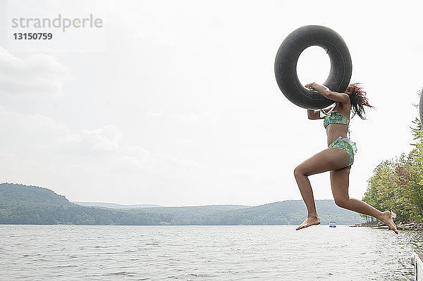 Junge Frau springt mit aufblasbarem Ring in den See