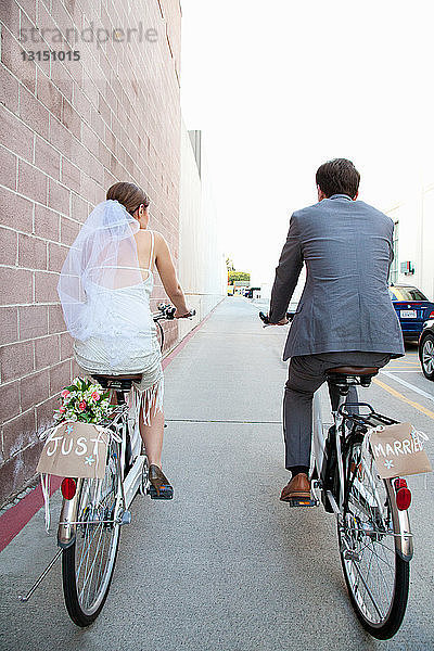 Junges  frisch verheiratetes Paar auf dem Fahrrad entlang der Straße  Rückansicht