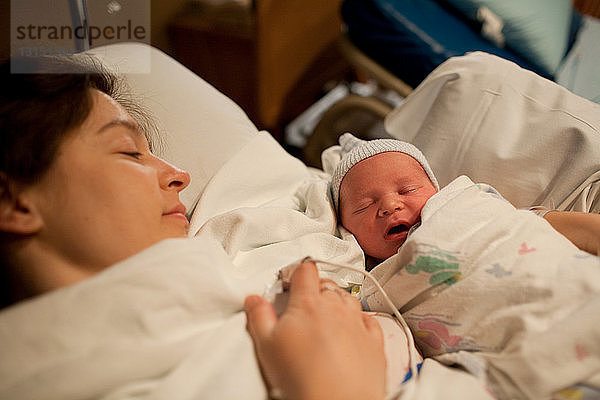 Mutter hält neugeborenen Jungen im Krankenhausbett