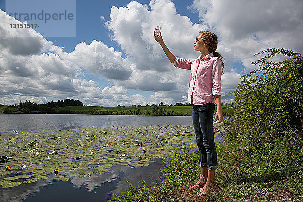 Teenager-Mädchen hält Glasgefäß neben dem See hoch