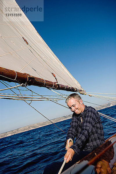 Mann lächelnd auf einem Segelboot sitzend