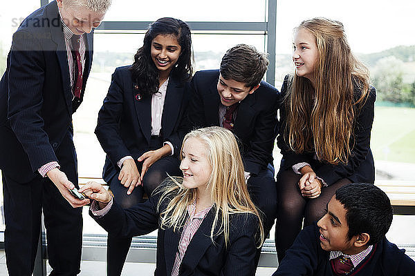 Gruppe von Schulkindern im Teenageralter mit Blick auf ein Mobiltelefon