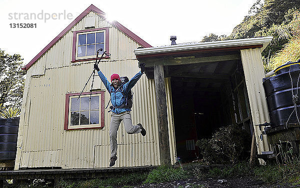 Wanderin springt mitten in der Luft vor einem Haus  Tararua Ridge  Neuseeland