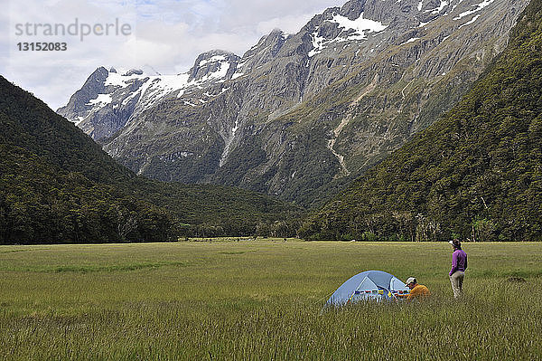 Paar zeltet auf einem Feld mit Bergen  Neuseeland
