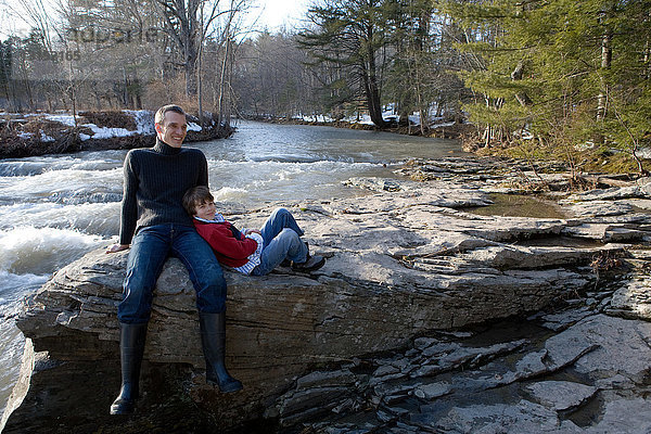 Vater und Sohn sitzen auf Felsen am Fluss