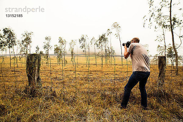 Mittlerer erwachsener Mann  der ein Feld mit Setzlingen fotografiert