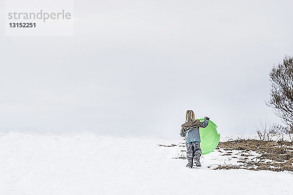 Rückansicht eines Kindes mit Schlitten im Schnee