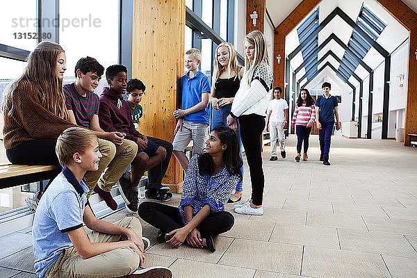 Gruppe von Schulkindern im Teenageralter  die im Korridor sitzen und sich unterhalten