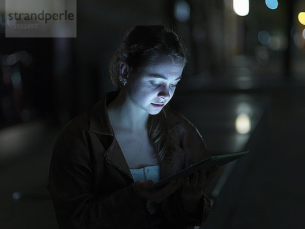 Junge Frau  die ein digitales Tablet benutzt  im Freien  bei Nacht  Gesicht beleuchtet