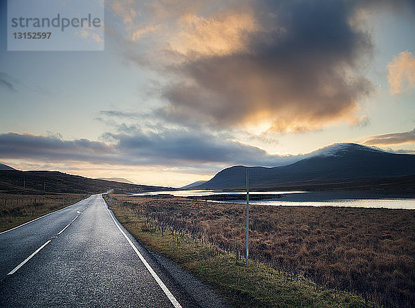 Blick auf eine ländliche Straße zu einem See bei Sonnenuntergang  Assynt  nordwestliche Highlands  Schottland  UK