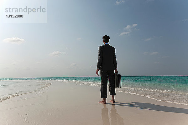 Geschäftsmann  der am tropischen Strand spazieren geht