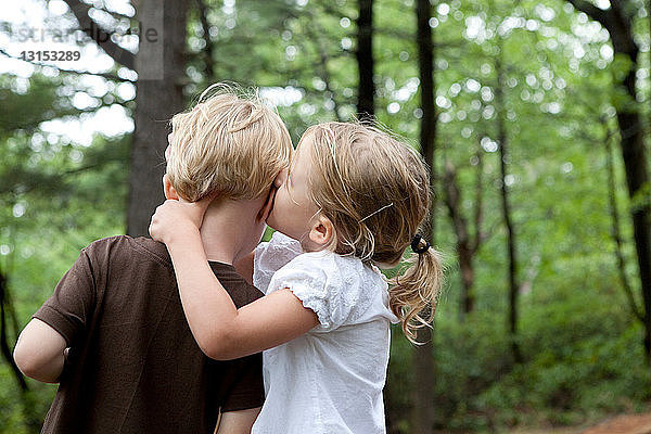 Mädchen flüstert ihrem Freund im Wald etwas zu