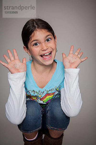 Studio-Porträt eines hockenden Mädchens mit erhobenen Händen