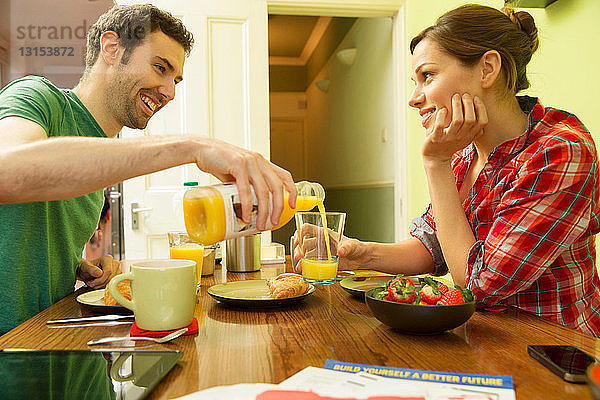 Junges Paar beim Frühstück  Mann schenkt Orangensaft ein