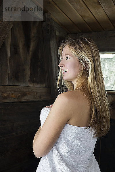 Junge Frau steht in der Sauna  eingewickelt in ein weißes Handtuch