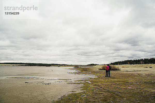 Zwei junge Erwachsene beim Wandern  stehen am See und betrachten die Aussicht