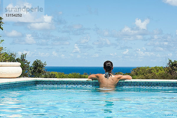 Rückansicht einer jungen Frau im Schwimmbad  mit Blick auf die Aussicht