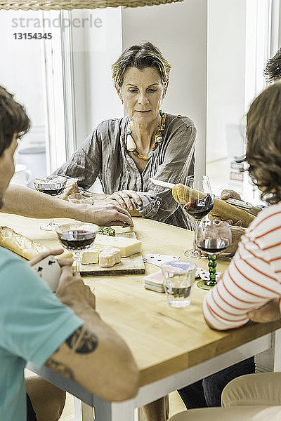 Erwachsene Freunde spielen Karten und trinken Wein am Esstisch