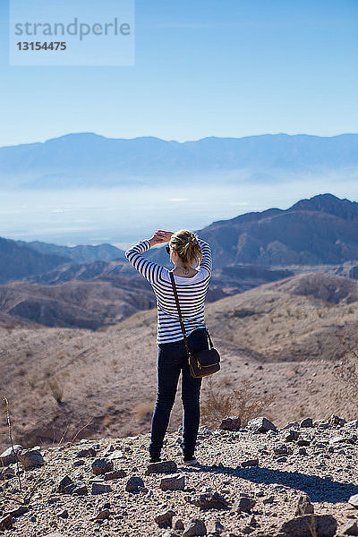 Junge Frau auf Felsen stehend  mit Blick auf die Berge  Rückansicht