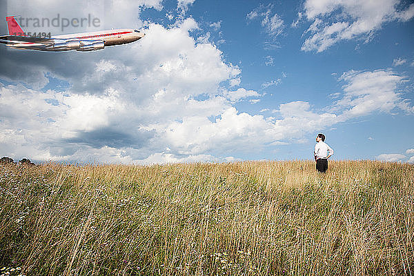Geschäftsmann im Feld mit Blick auf ein Flugzeug