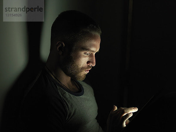Junger Mann  der nachts sein Smartphone benutzt  Gesicht beleuchtet