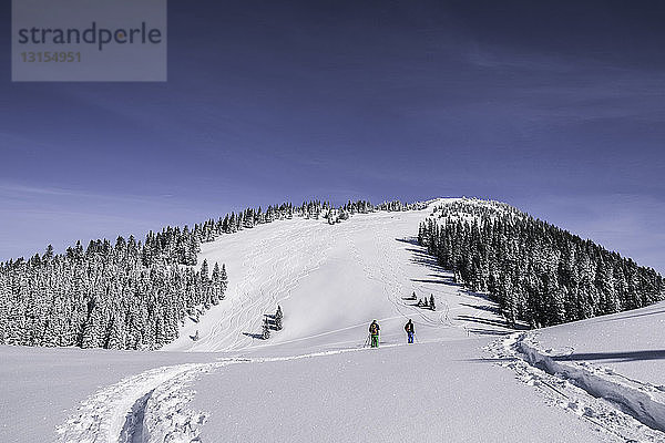 Entfernte Ansicht von zwei männlichen Skifahrern  die einen schneebedeckten Berg hinaufgehen  Spitzingsee  Deutschland