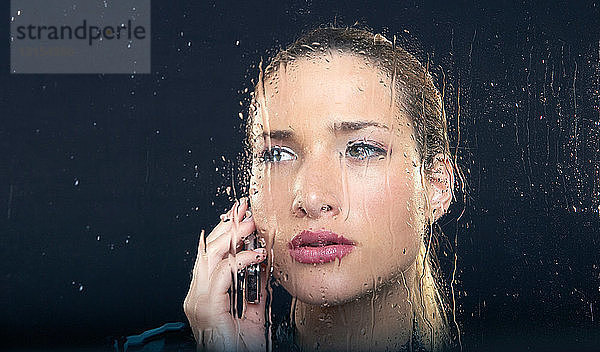 Frau am regnerischen Fenster mit Telefon