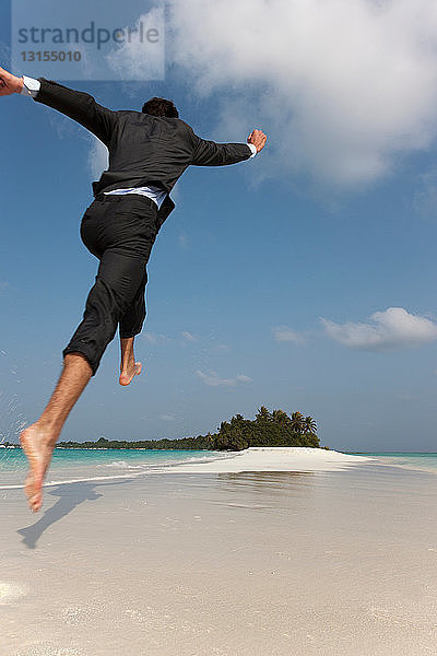 Geschäftsmann springt am tropischen Strand