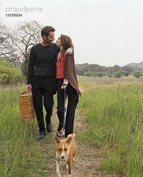 Ehepaar mit Picknickkorb geht mit Hund spazieren