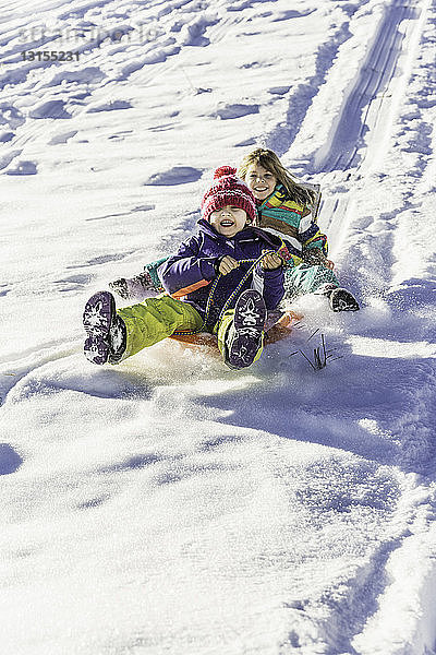 Mädchen fahren mit dem Schlitten einen schneebedeckten Hang hinunter  Achenkirch  Tirol  Österreich